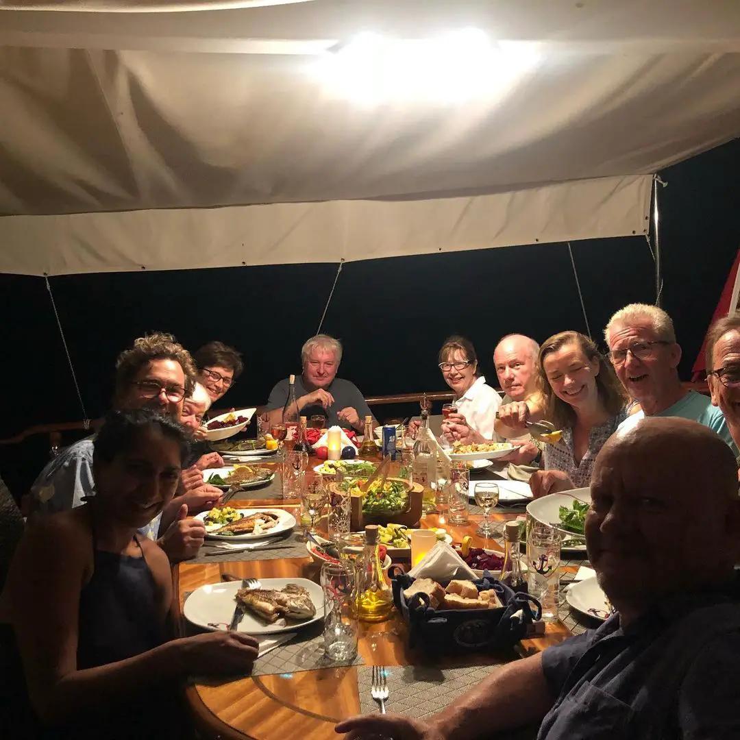 group of guests enjoying dinner together at yacht dining table with food and wine