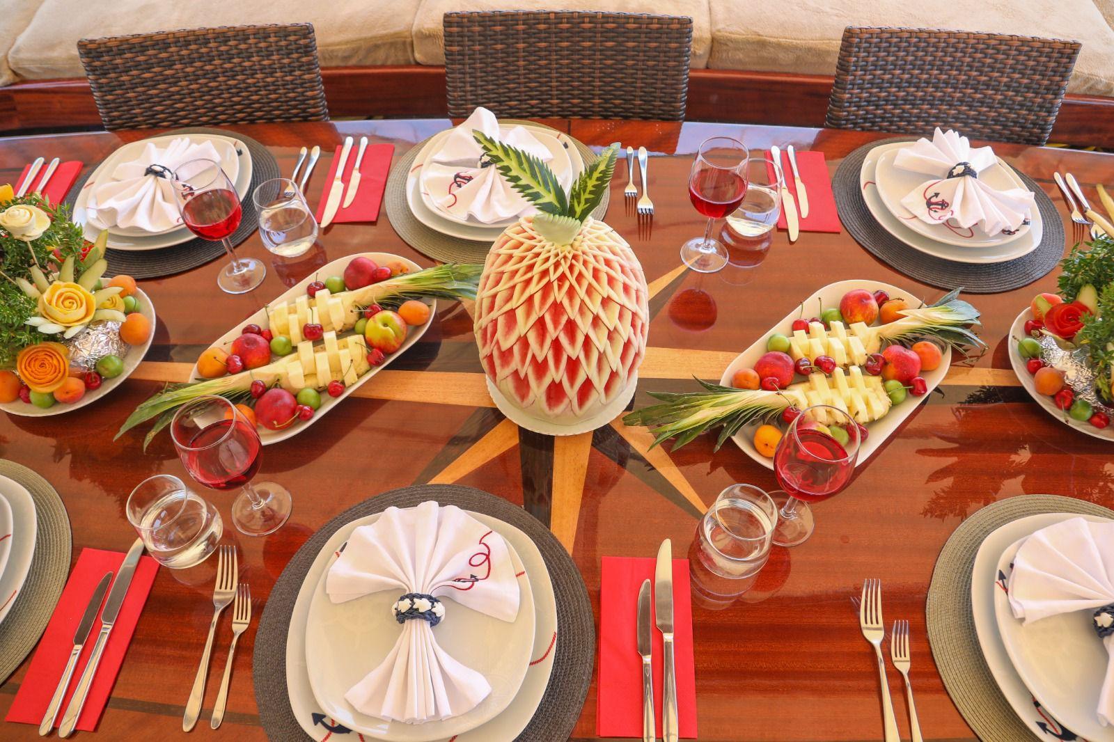 elegant yacht dining table with carved pineapple centerpiece, fruit platters, wine glasses and formal place settings