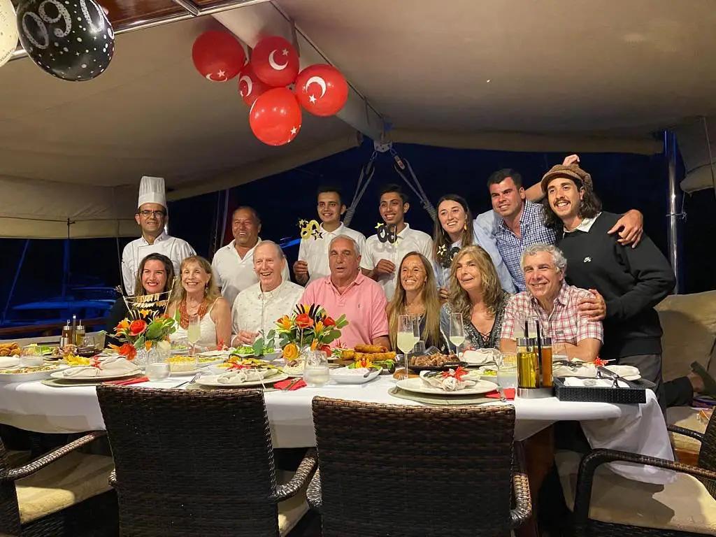 yacht dining celebration with guests seated at formal dinner table with food, crew and chef posing together