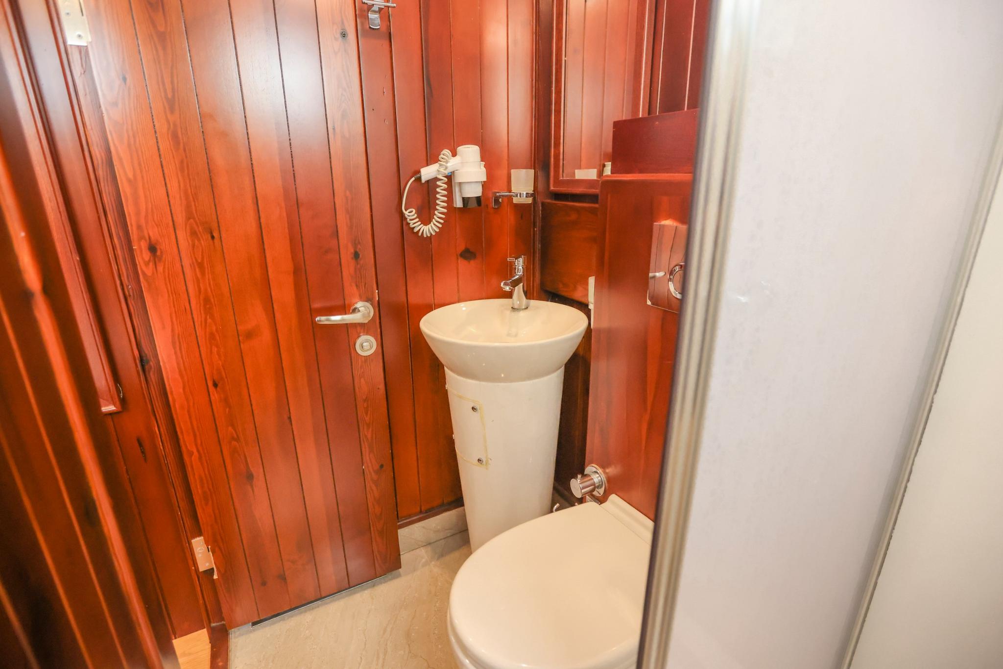 yacht bathroom with white pedestal sink, toilet, mirror and rich wood paneling