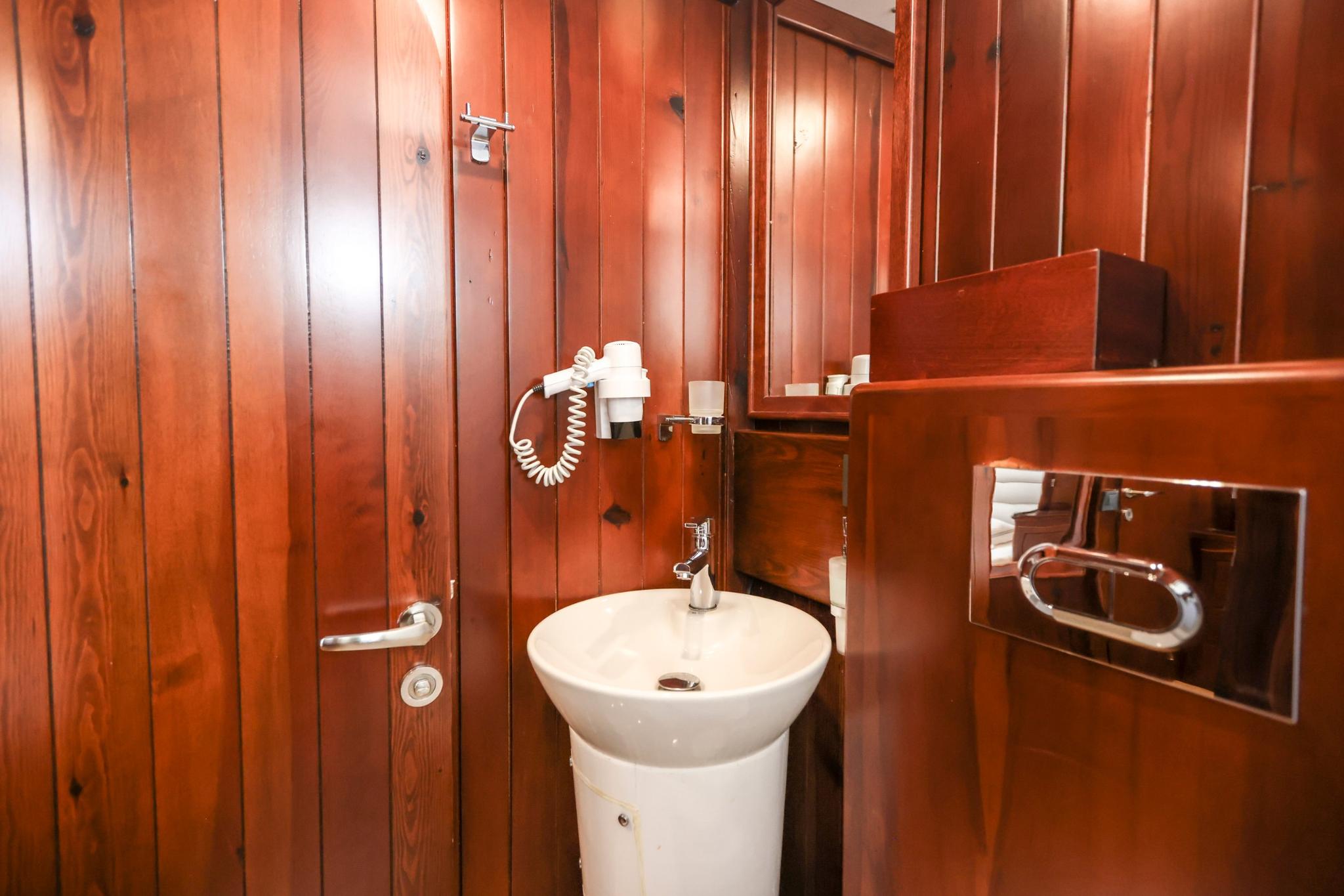 Yacht bathroom featuring white pedestal sink, rich wood paneling, wall-mounted hair dryer and mirror