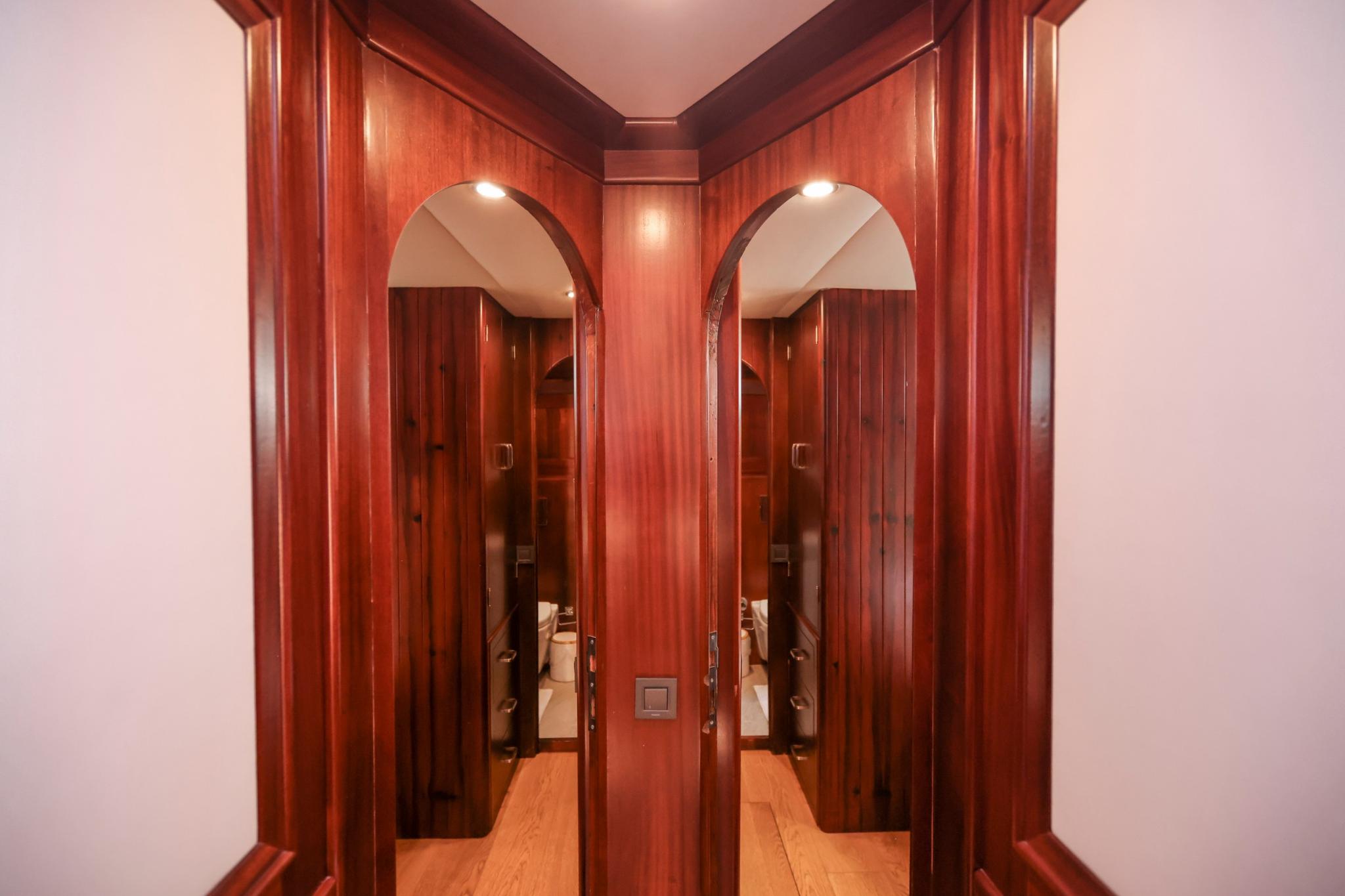 yacht interior corridor with rich wood paneling and arched doorways to guest cabin bathrooms