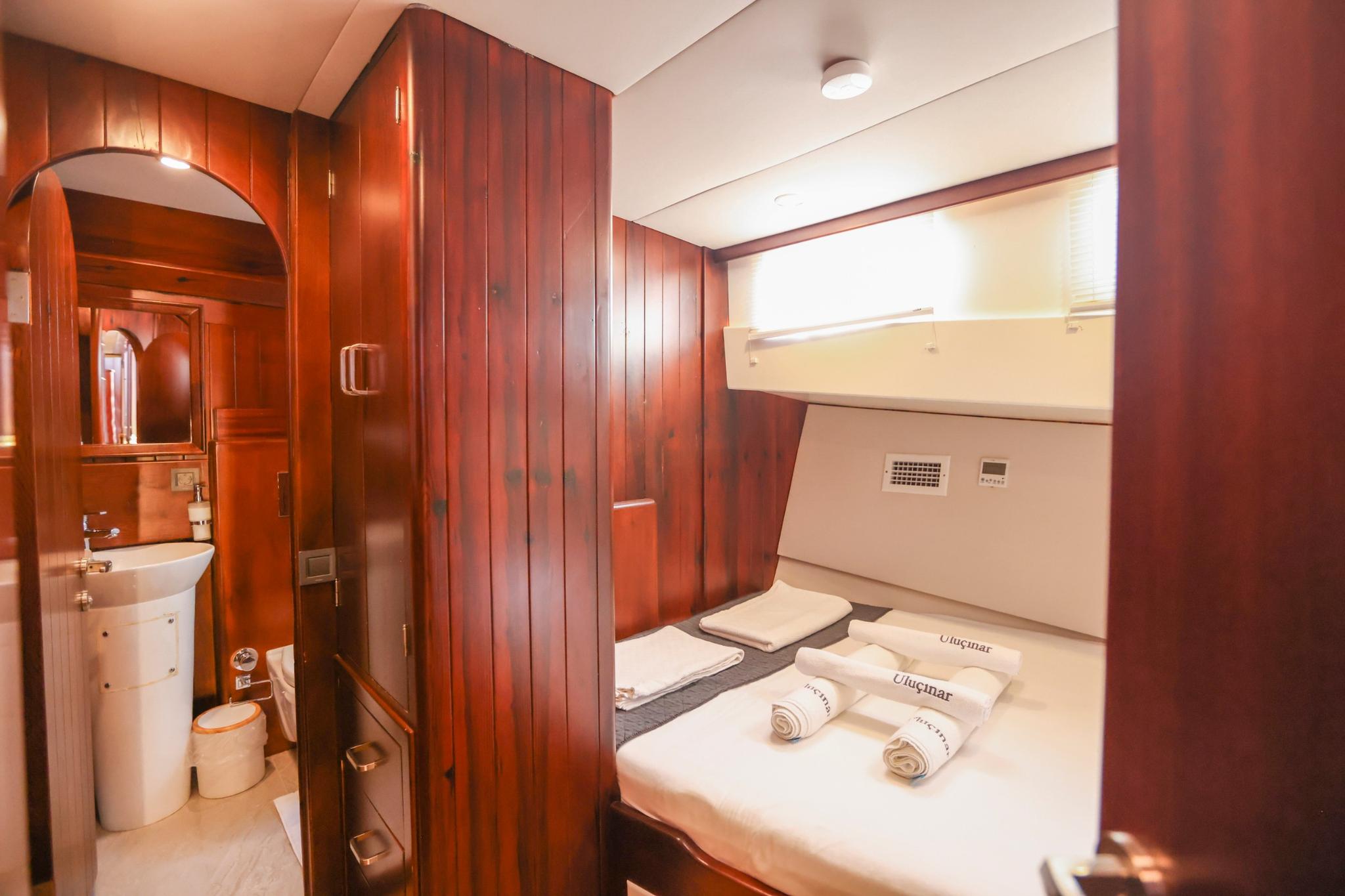 yacht guest cabin with single bed, wooden paneling and ensuite bathroom with basin