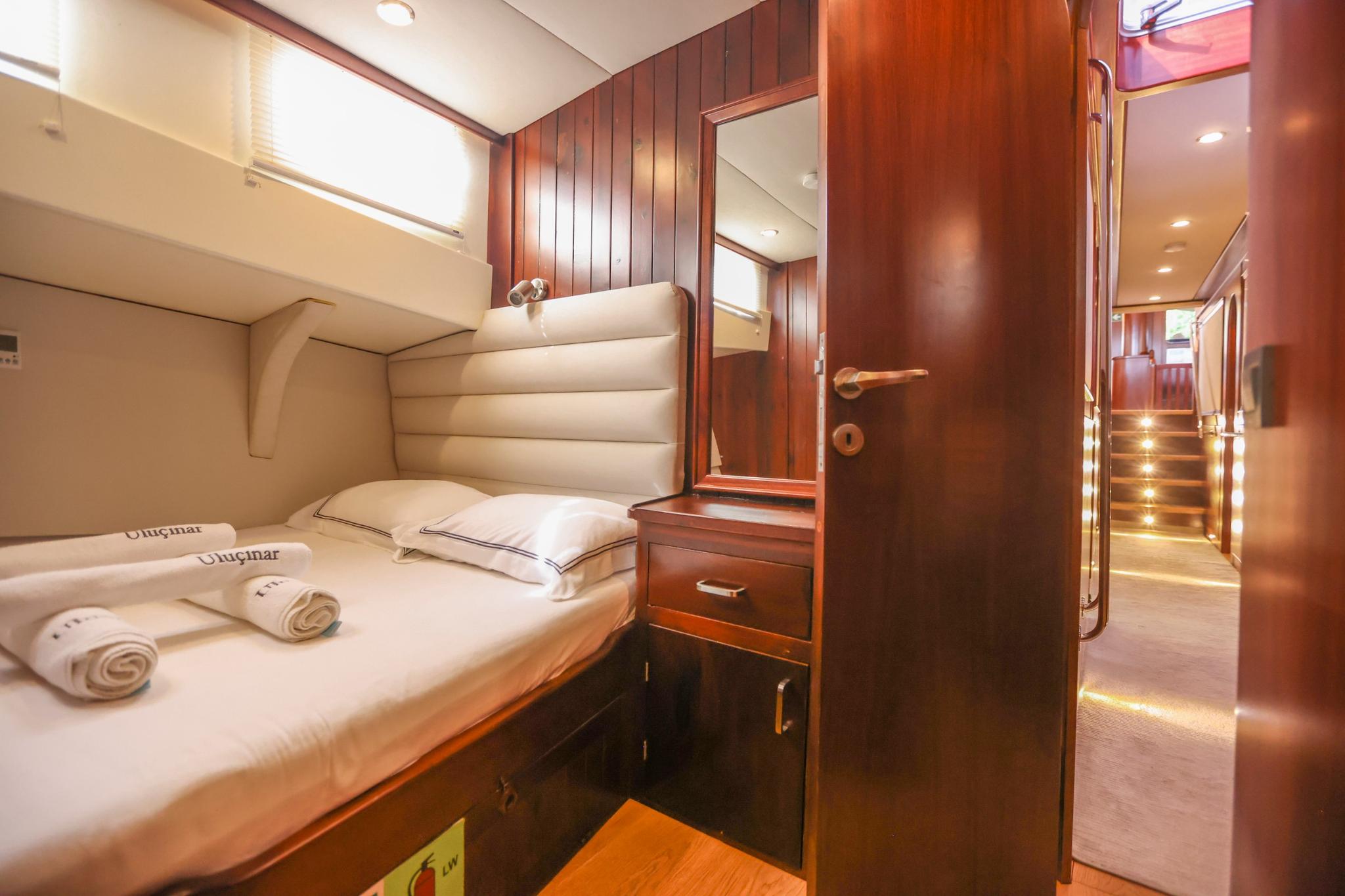 yacht guest cabin featuring single bed with beige upholstered headboard and rich mahogany woodwork