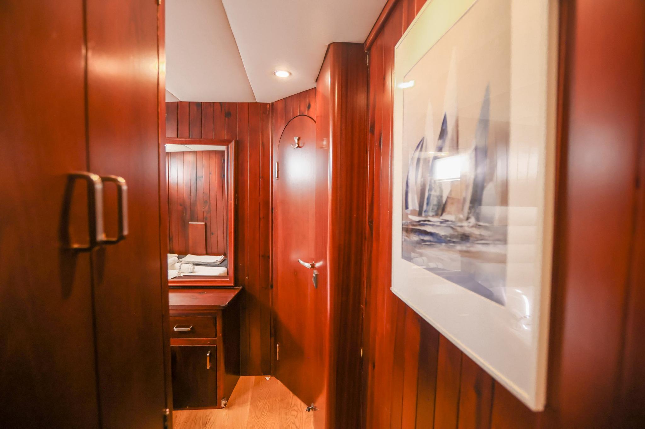 yacht cabin corridor with rich wood paneling, ensuite bathroom entrance and nautical artwork