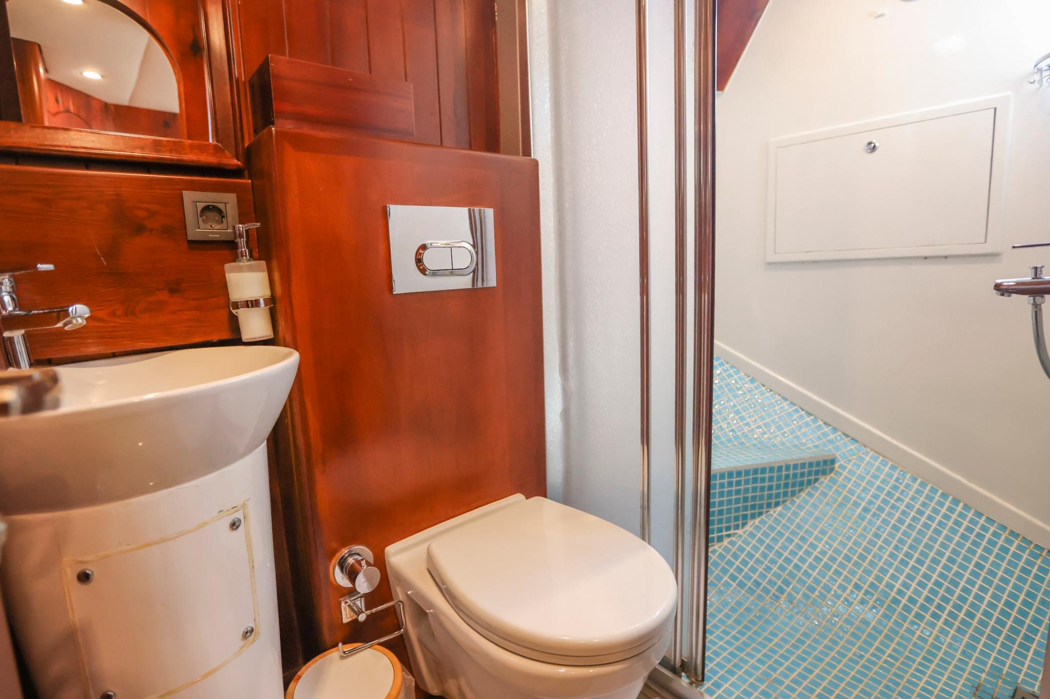 yacht bathroom featuring white toilet, vessel sink, rich wood paneling and blue mosaic tile shower