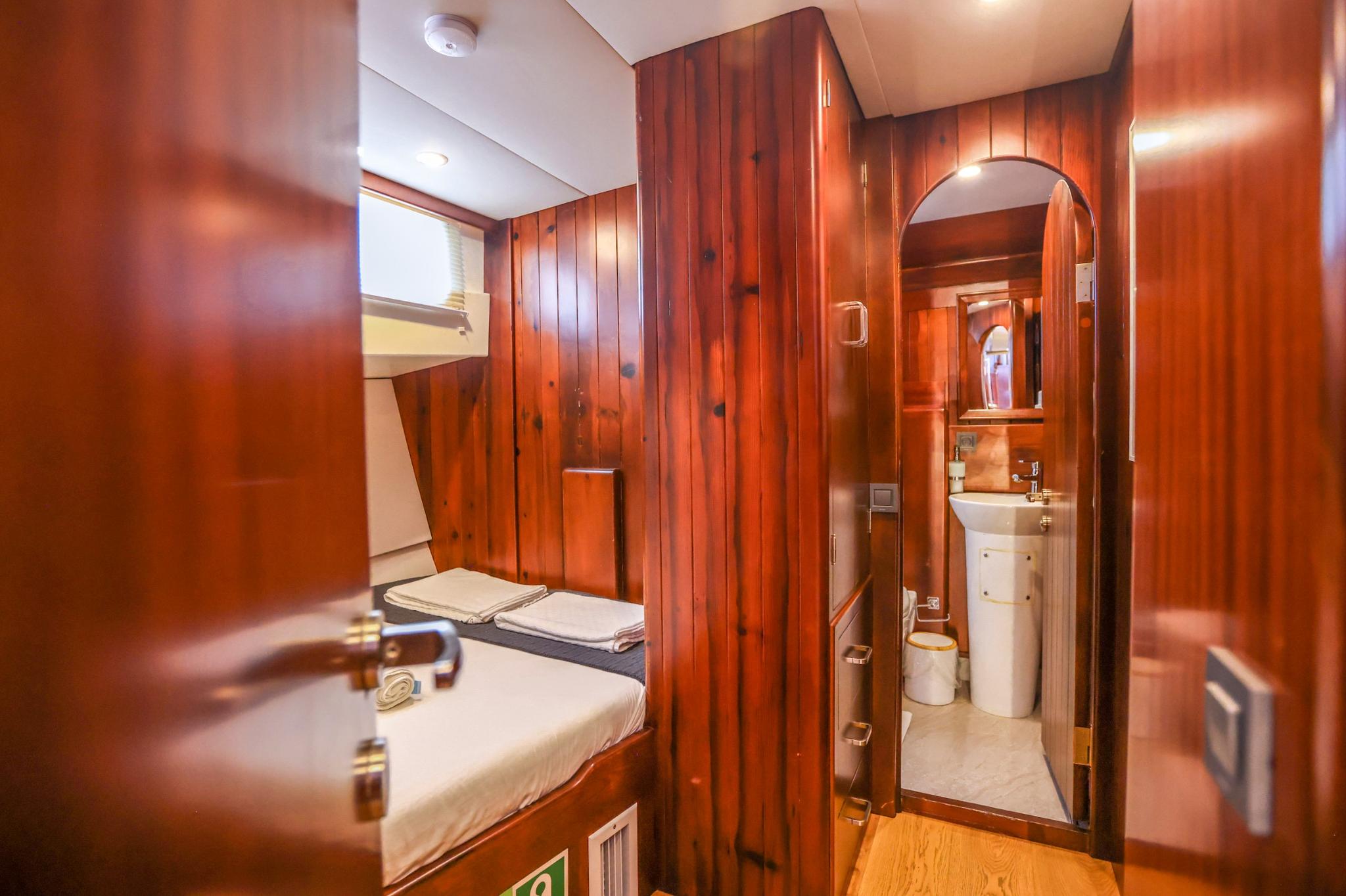 yacht guest cabin with single bed, wood paneling and adjoining bathroom with sink