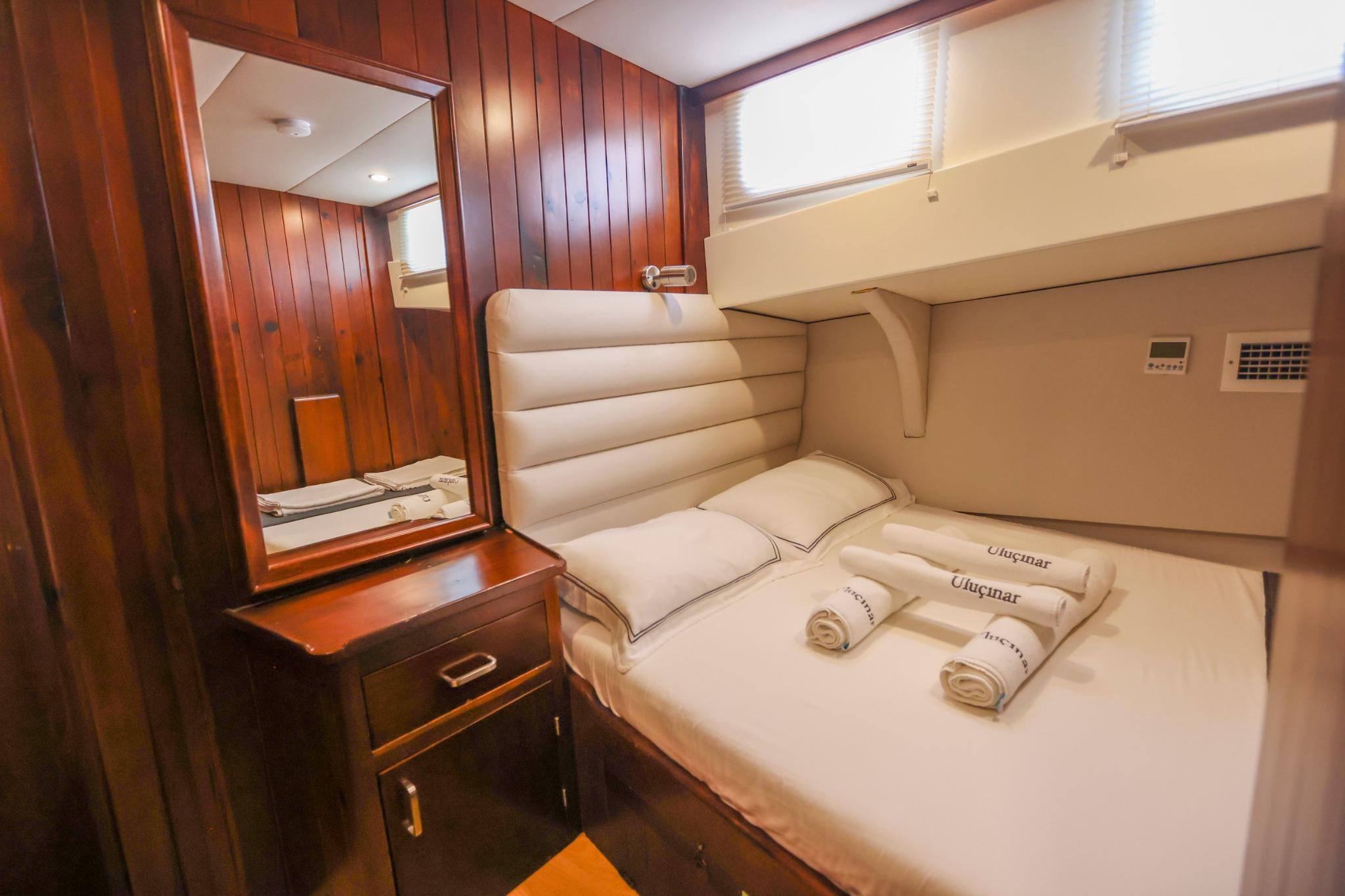 yacht guest cabin featuring double bed with cream upholstery, wooden vanity with mirror and porthole windows