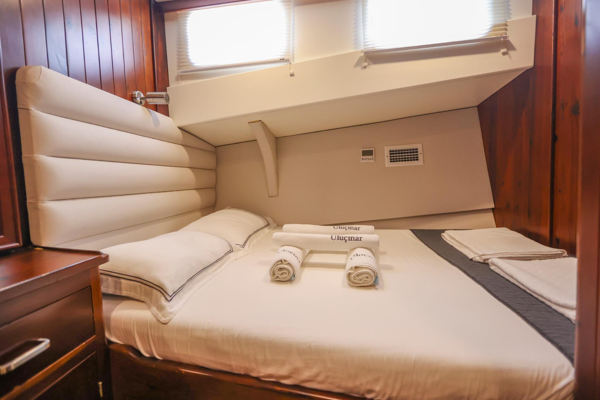 yacht guest cabin with double bed, cream linens, rolled towels and side portholes