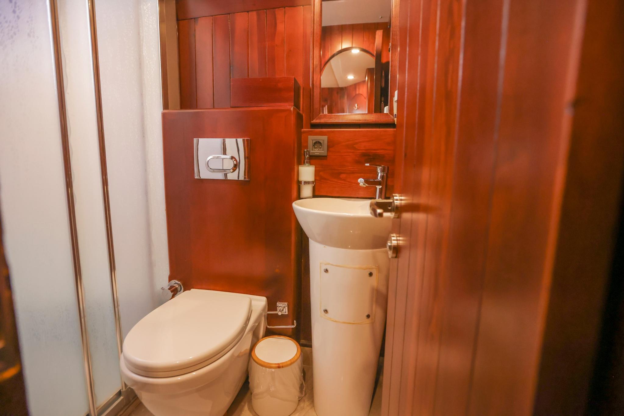 yacht bathroom with white toilet, pedestal basin, mirror and rich wood paneling