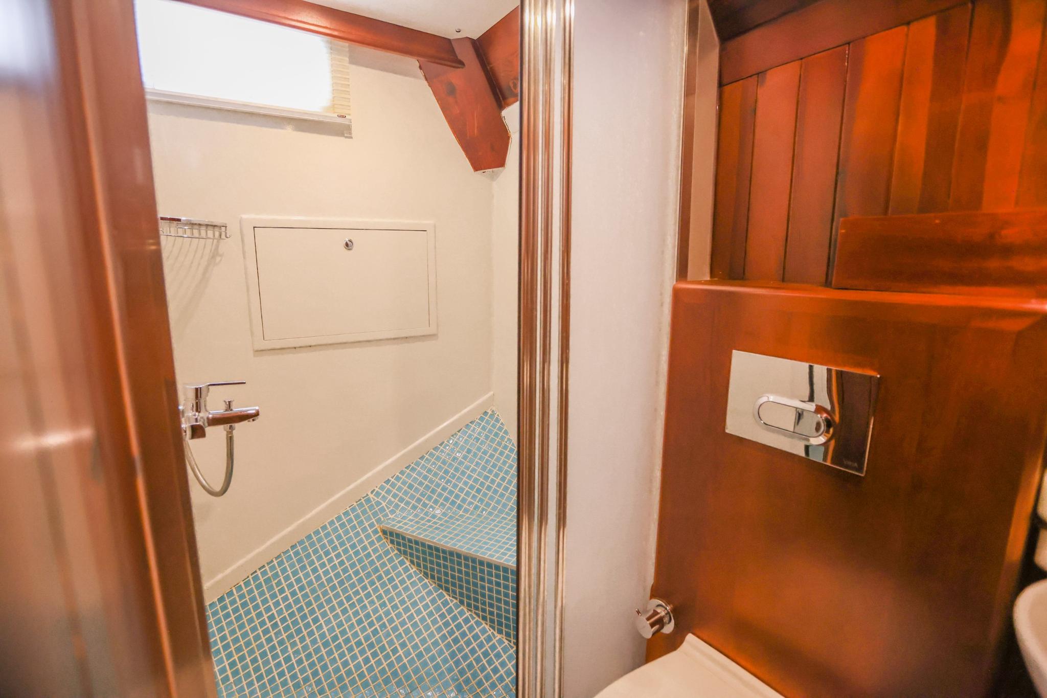 yacht bathroom featuring blue mosaic tiled shower area with chrome fixtures and teak cabinetry