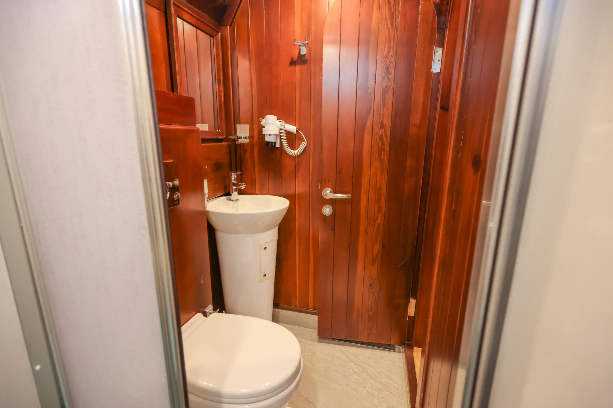 Small yacht bathroom featuring white toilet and pedestal sink with rich wood paneling