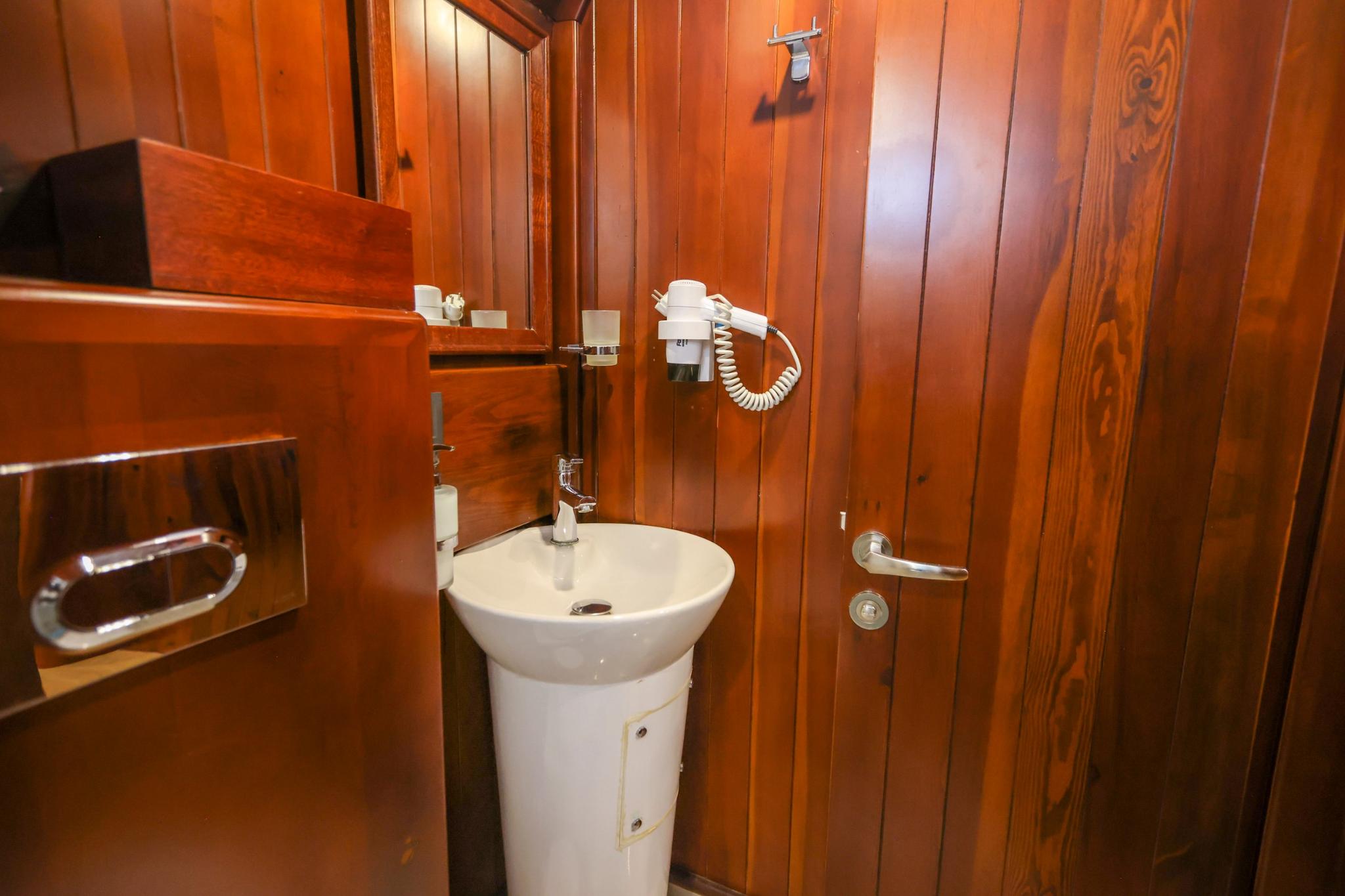 yacht bathroom featuring white pedestal sink, wall-mounted hair dryer, and rich wood paneling throughout
