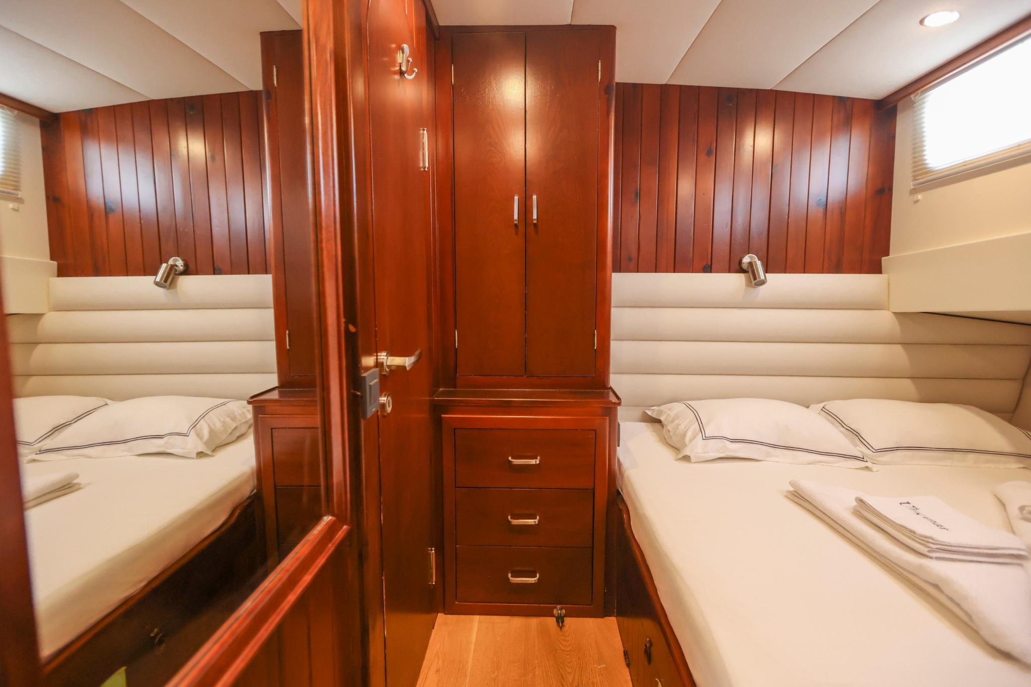 yacht guest cabin featuring twin beds with cream upholstery and central mahogany storage cabinet
