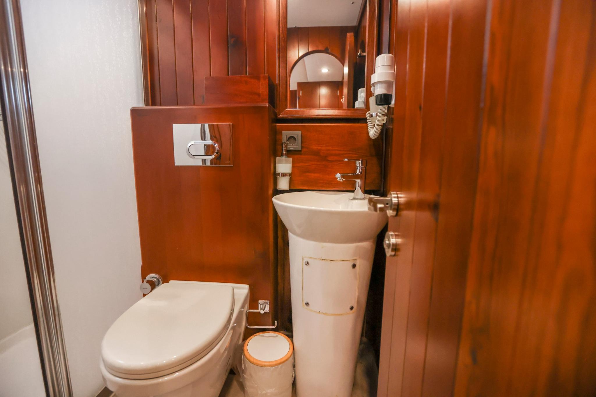 compact yacht bathroom featuring white toilet, pedestal basin, and rich wood paneling