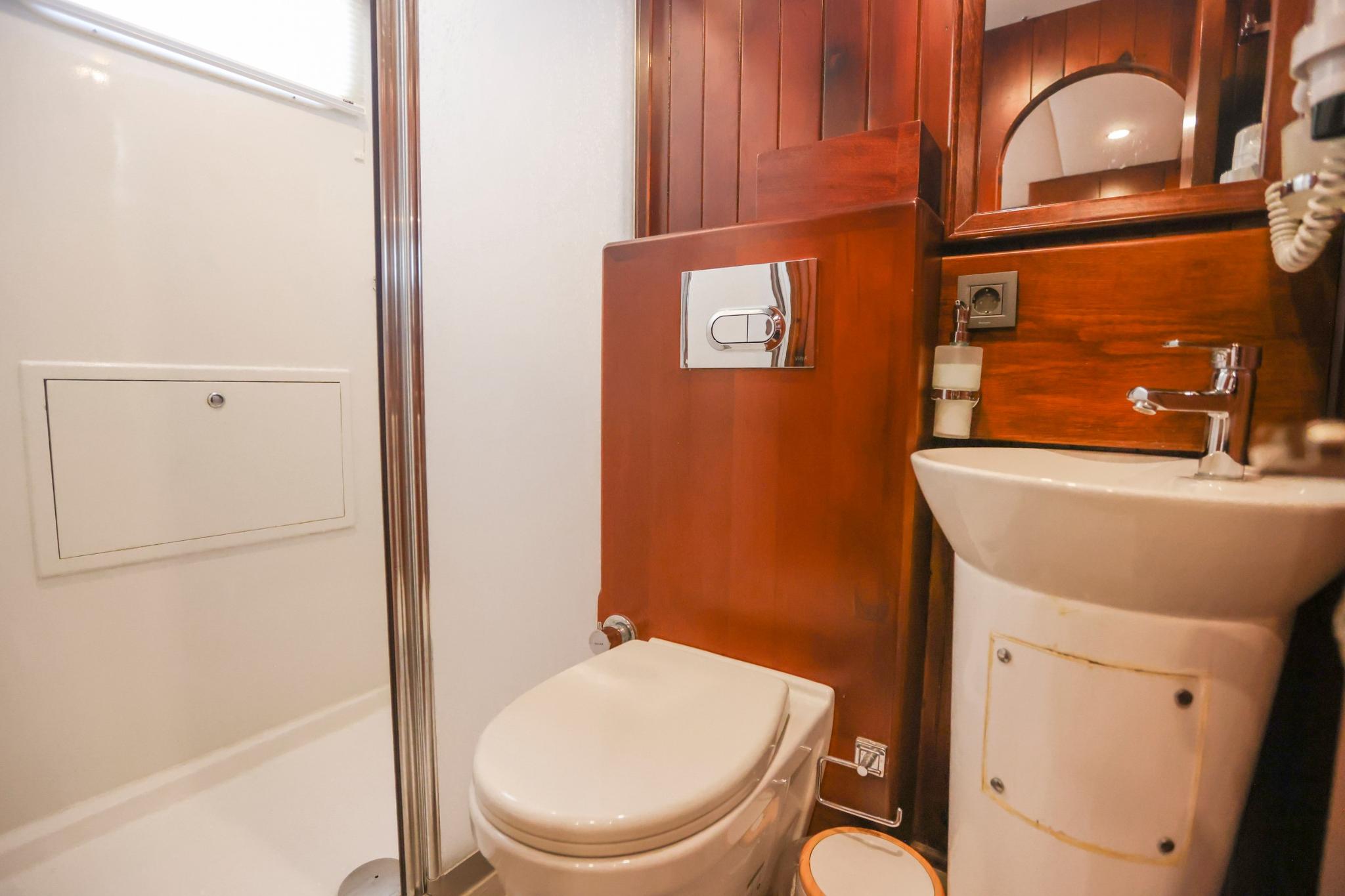 compact yacht bathroom with white toilet, washbasin, and warm wood paneling