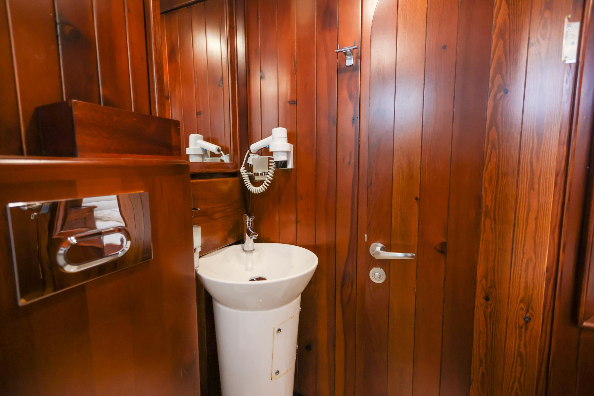 yacht bathroom interior with white pedestal sink, wall-mounted hairdryer, and wood paneling