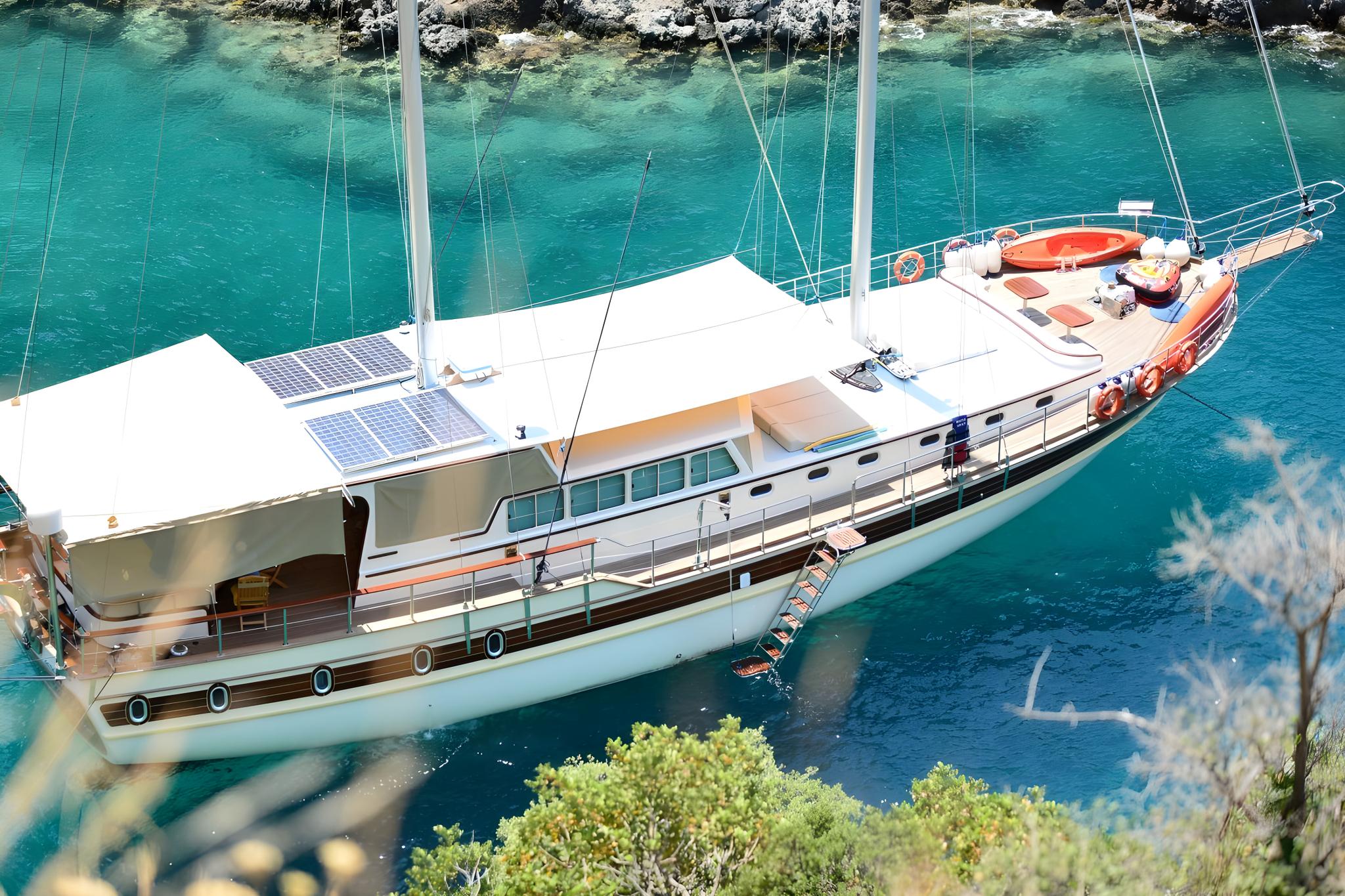 aerial view of white luxury gulet with solar panels anchored in crystal clear turquoise Mediterranean bay