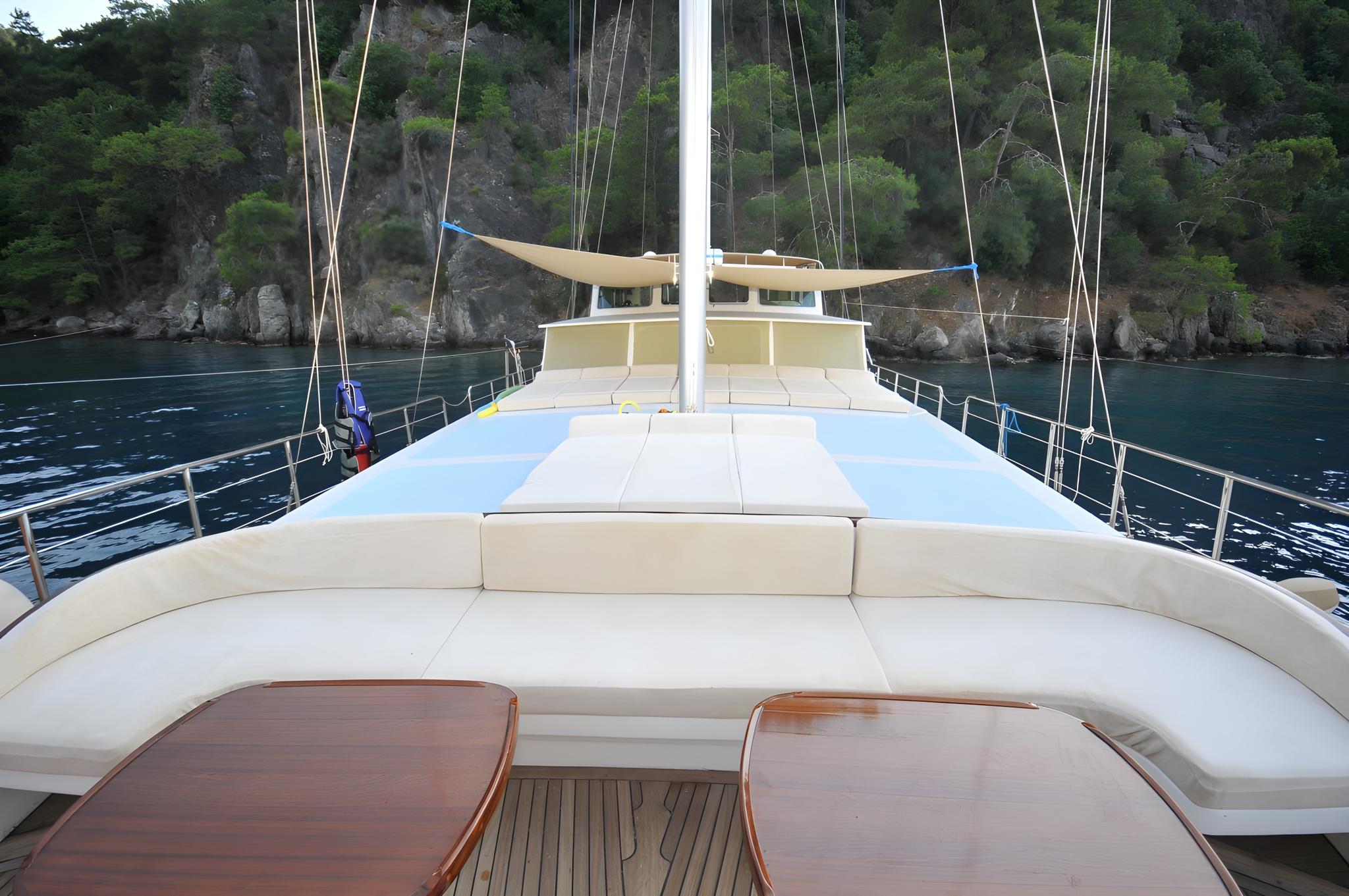 gulet forward deck with curved white cushioned seating and polished teak tables