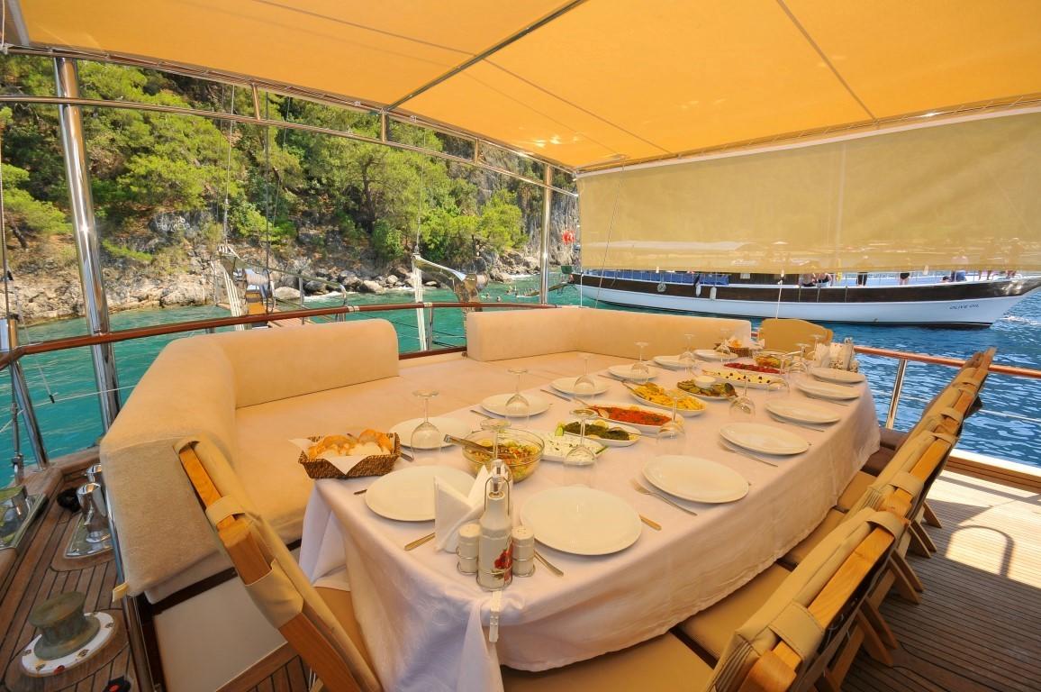 Covered aft deck dining area with white tablecloth, served dishes, and place settings overlooking turquoise bay