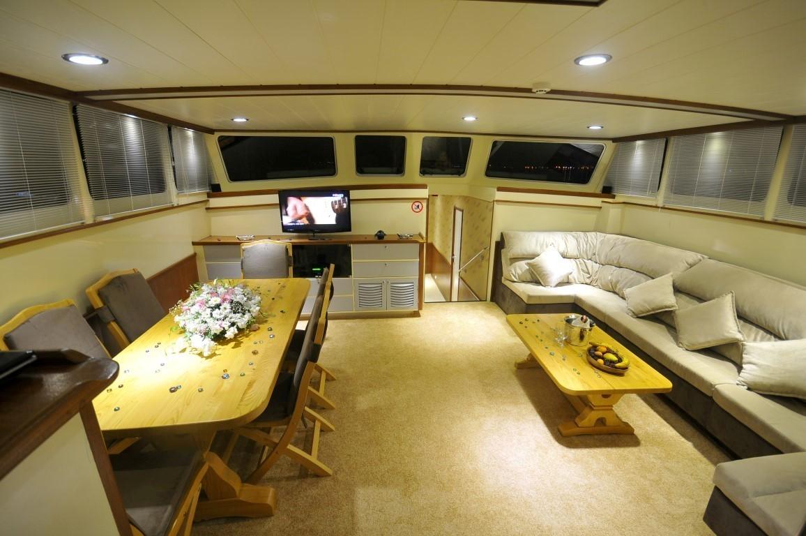 yacht cinema room with wall-mounted screen, curved seating, dining table and entertainment system