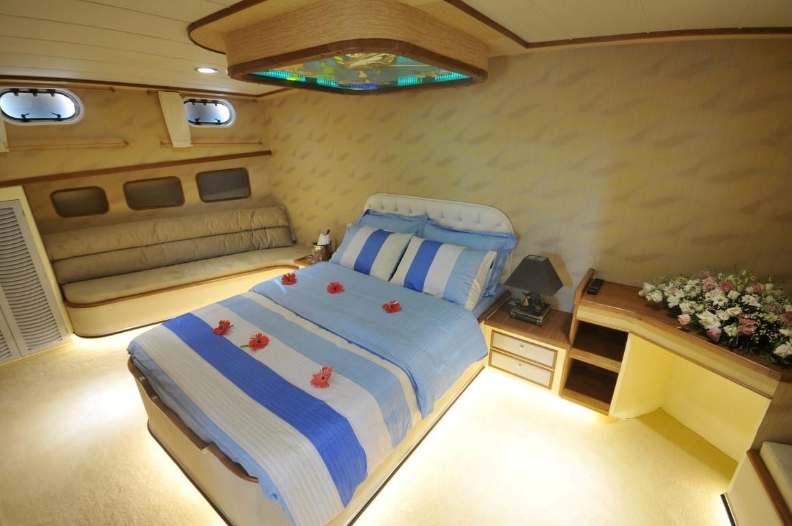 yacht guest cabin with blue striped bedding, wood paneling, portholes and ceiling mounted TV