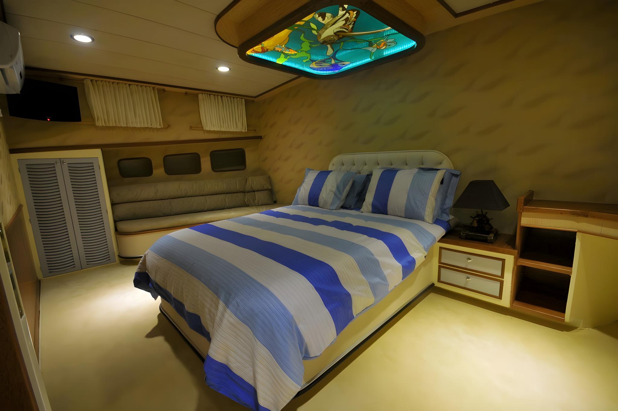 yacht cabin interior with double bed, blue striped bedding, built-in seating and decorative ceiling panel