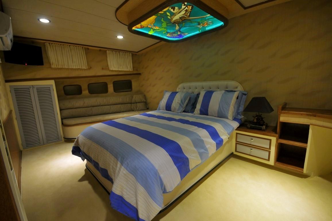 yacht cabin interior with double bed, blue striped bedding, built-in seating and decorative ceiling panel