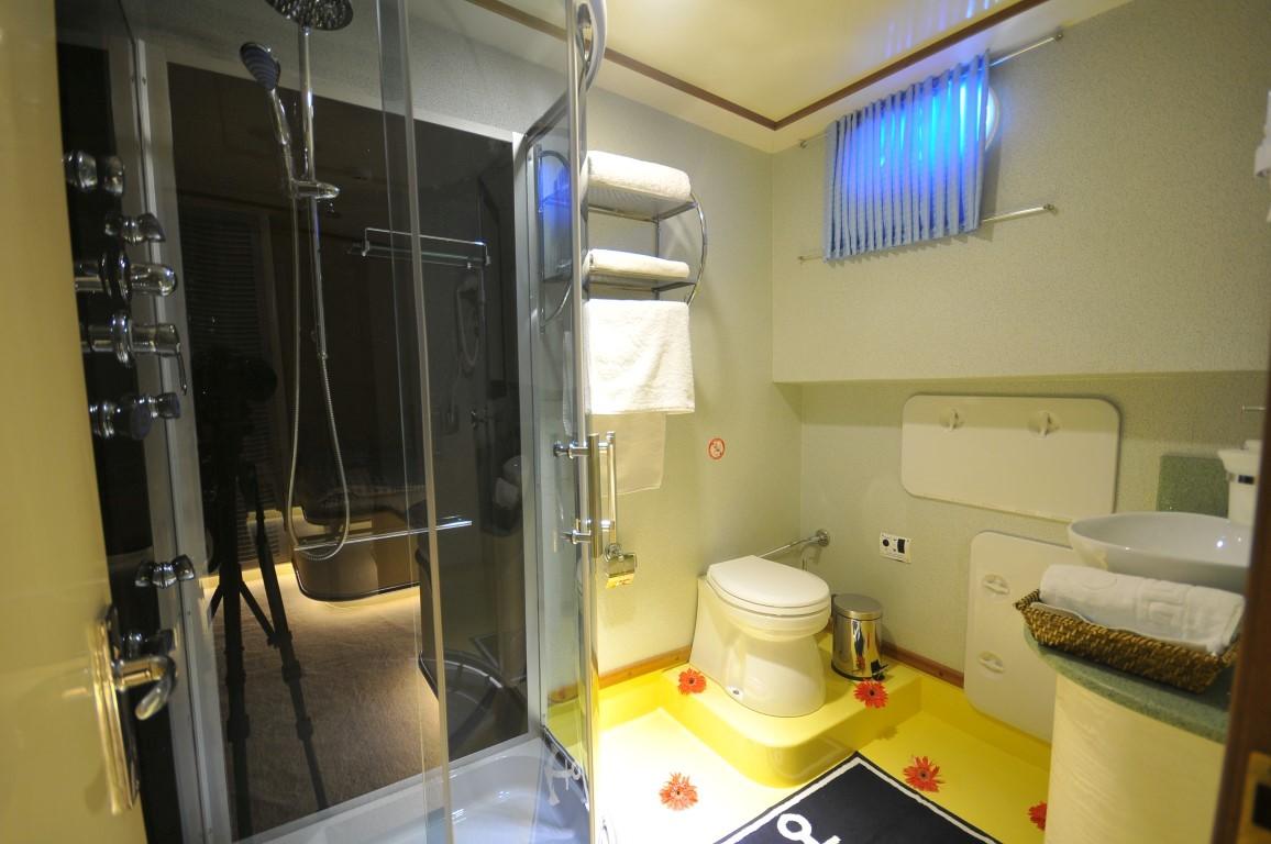 yacht bathroom featuring glass-enclosed shower, white toilet, and built-in storage with towels
