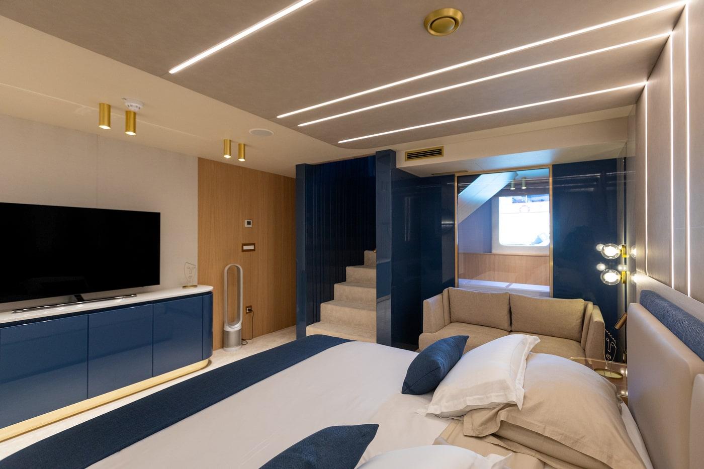 Luxury yacht master cabin featuring large bed with navy accents and entertainment system