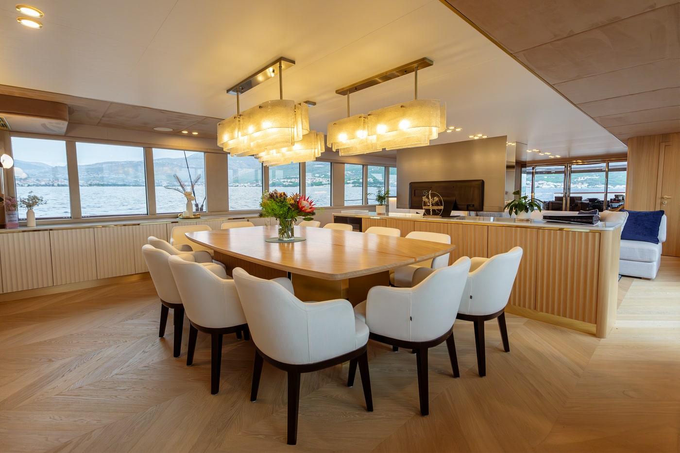 Luxury yacht main salon with dining table, galley kitchen and panoramic windows