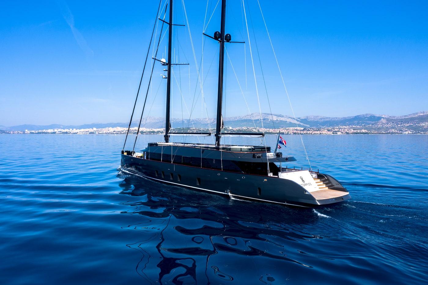 Luxury sailing yacht with dark hull and twin masts on calm blue water