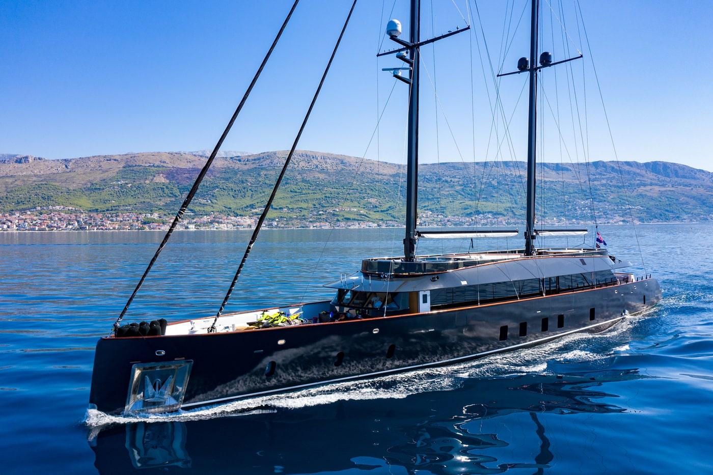 Large luxury sailing yacht with dark hull cruising on blue water