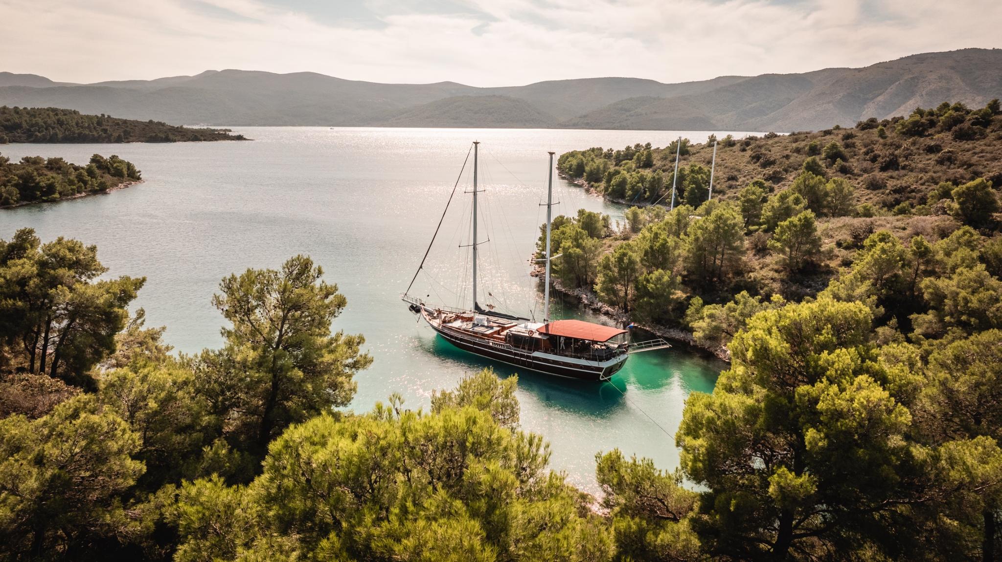 aerial view of traditional wooden gulet anchored in secluded turquoise bay surrounded by pine forest