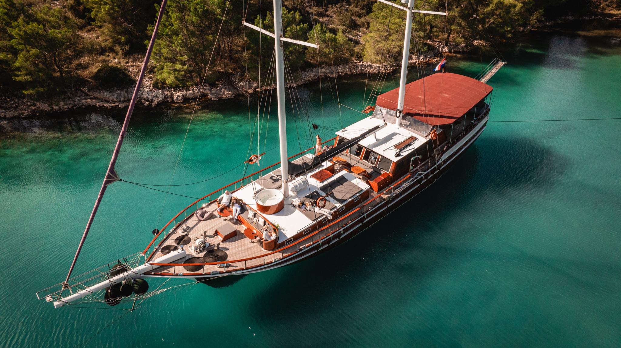 aerial view of wooden gulet yacht anchored in crystal clear turquoise bay with forested coastline
