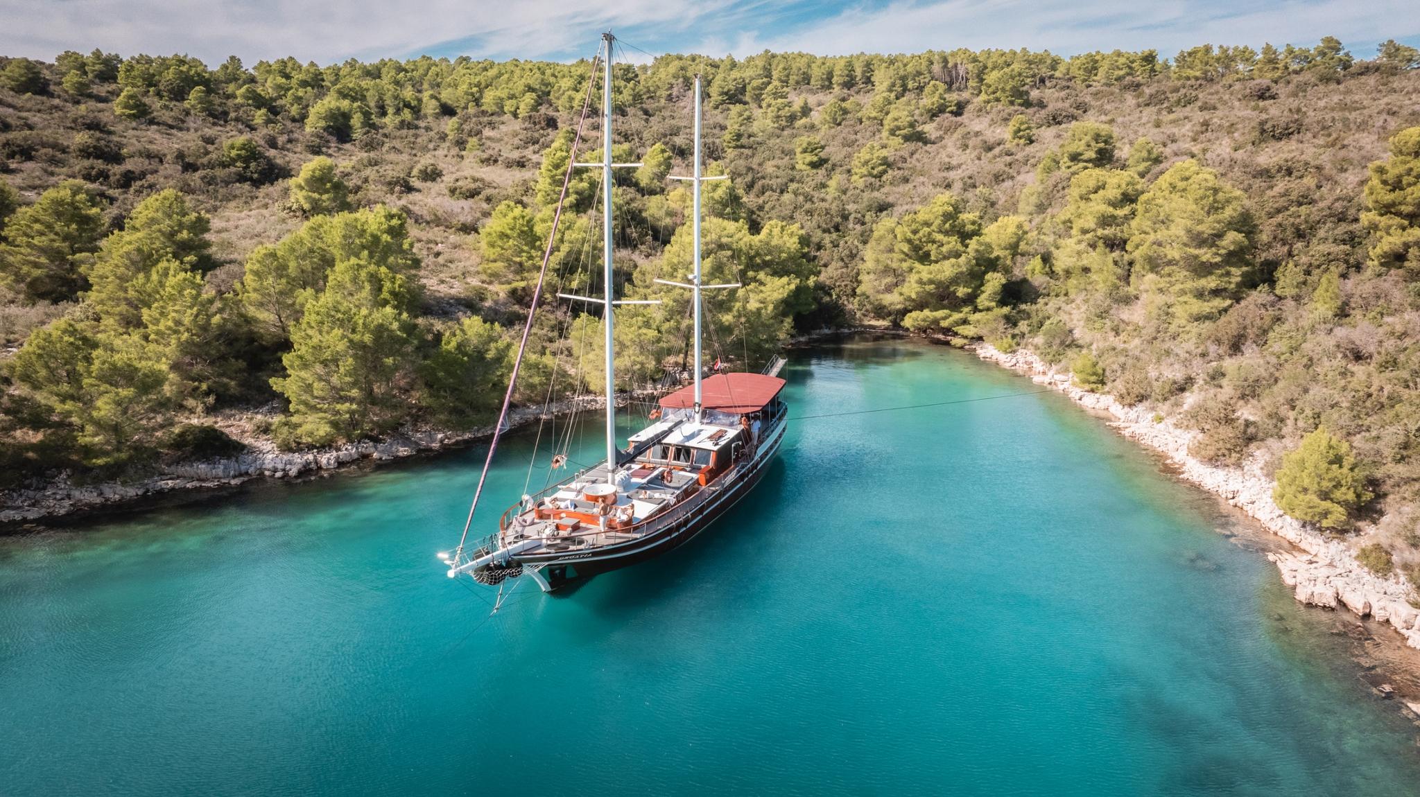 aerial view of traditional wooden gulet anchored in secluded turquoise bay surrounded by pine forest