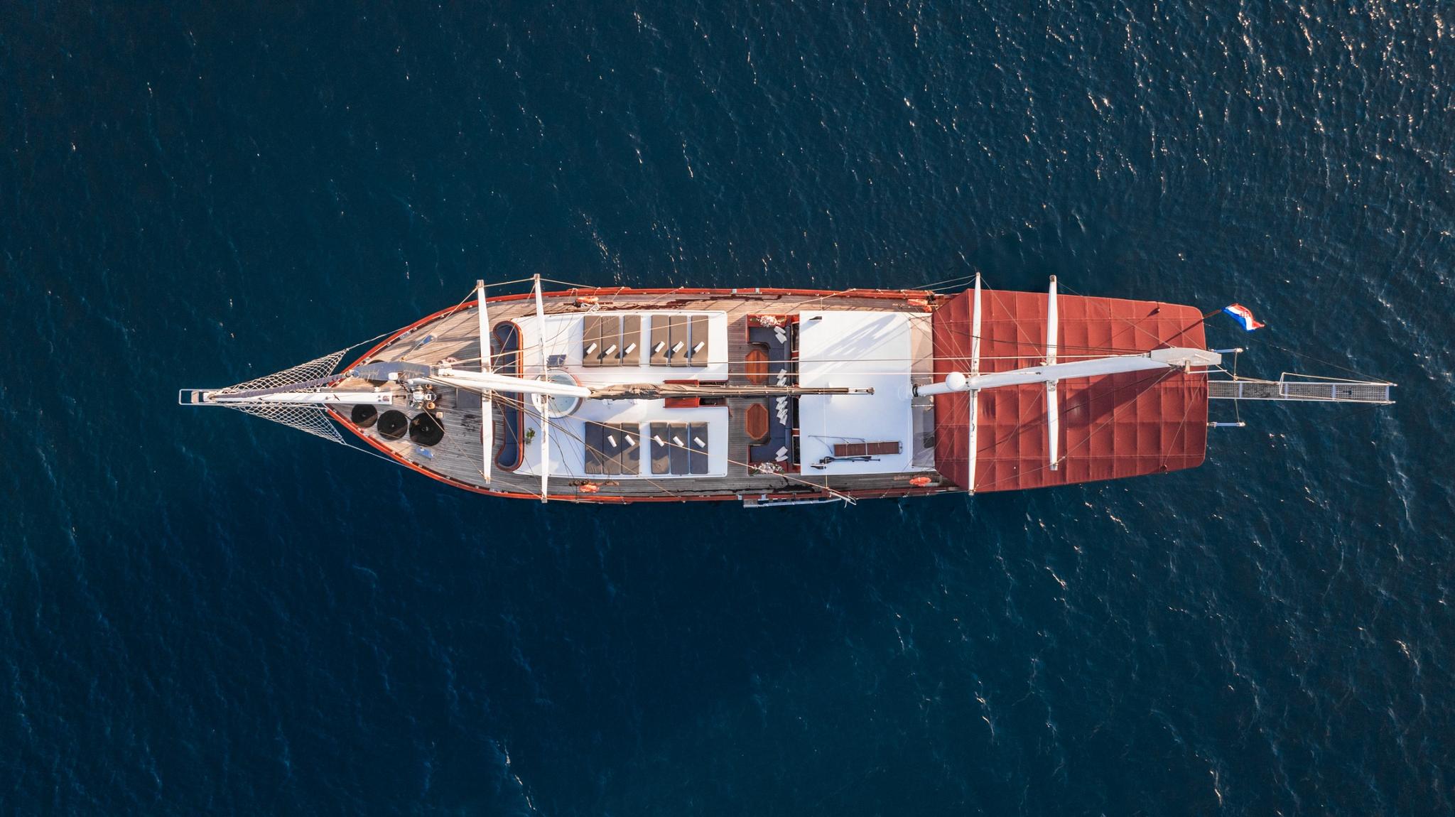 aerial view of classic sailing yacht with white hull and red awning at anchor
