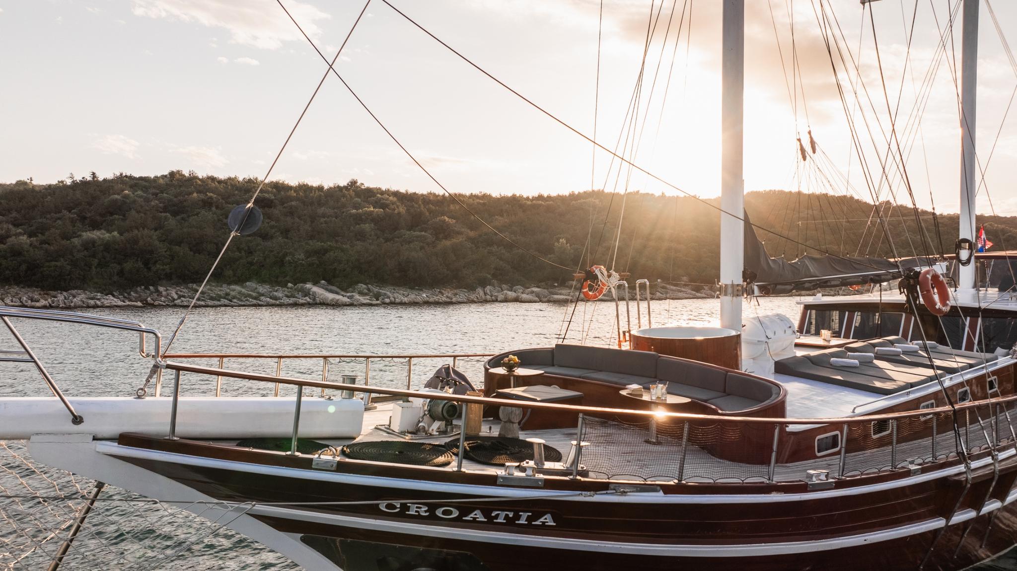 Traditional wooden gulet stern deck featuring curved seating area and mast rigging at golden hour