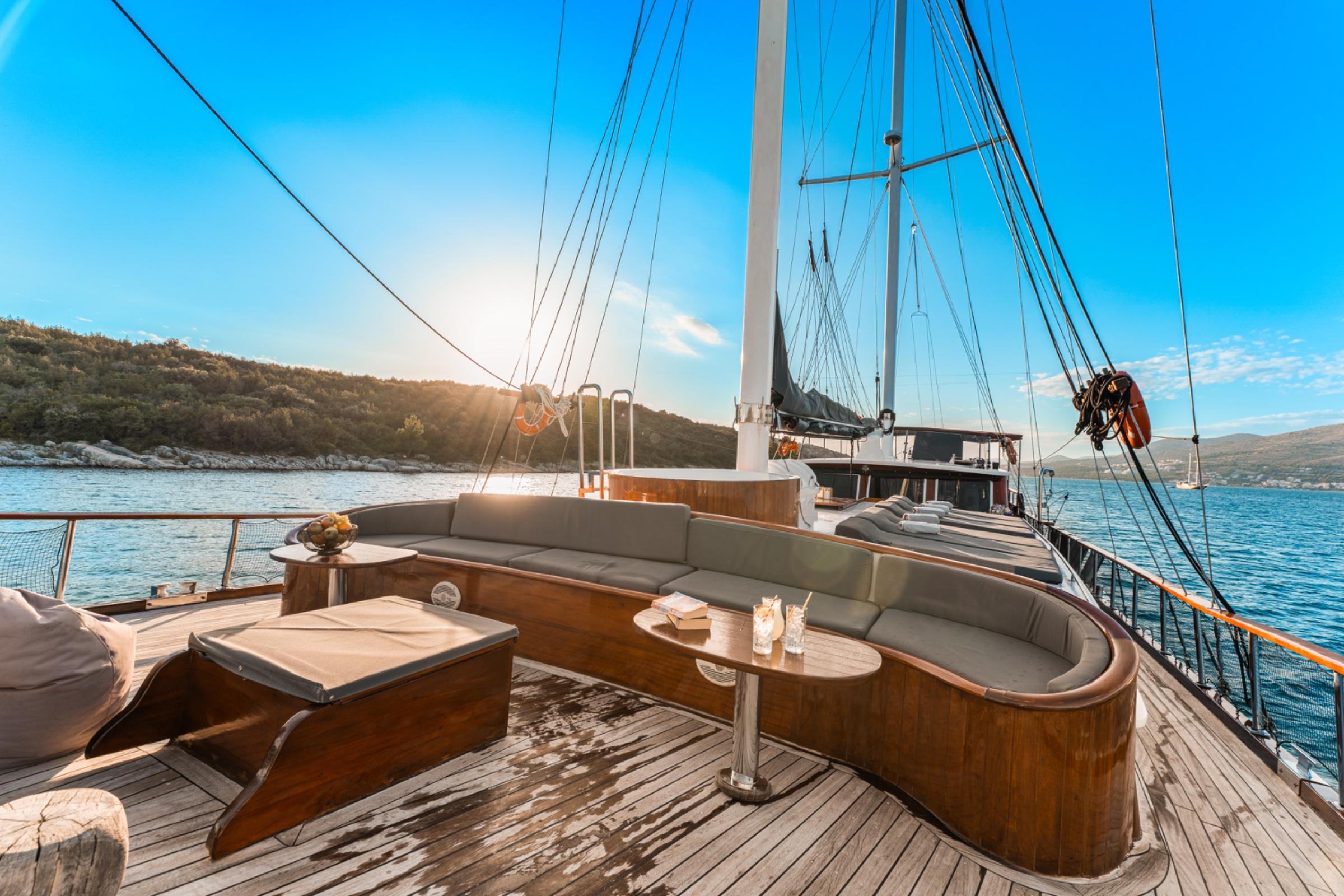bow deck seating area with curved gray banquette, teak table and wooden decking