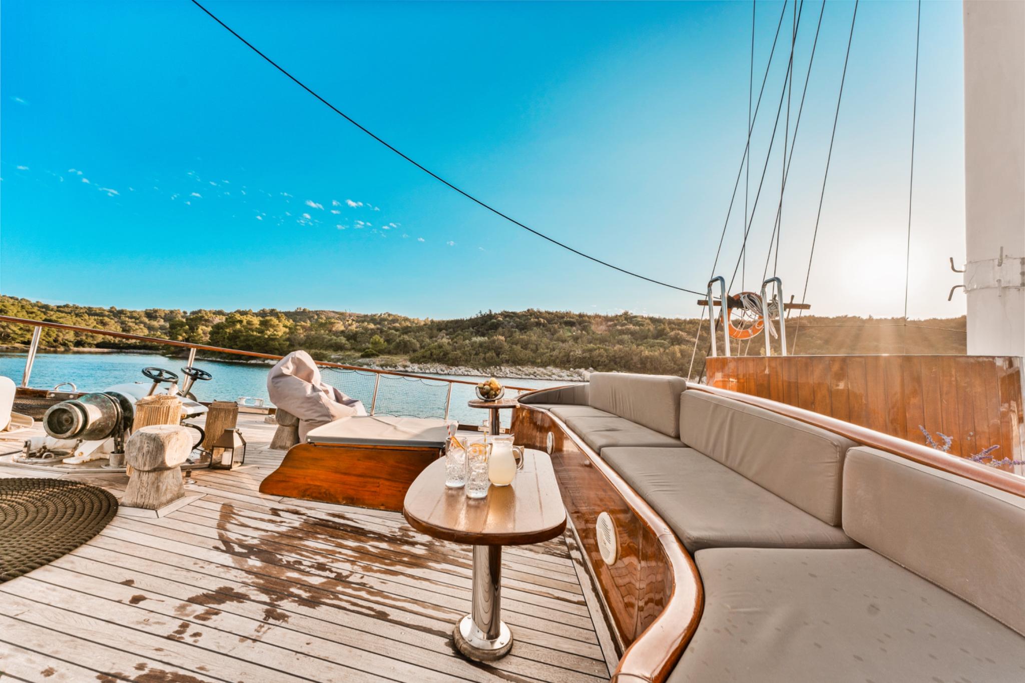 gulet aft deck with curved beige banquette seating, wooden table, and teak decking