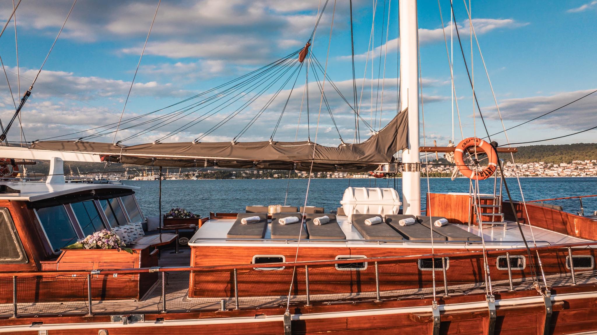 Traditional wooden gulet sun deck with dark cushioned sunbathing area and rigging