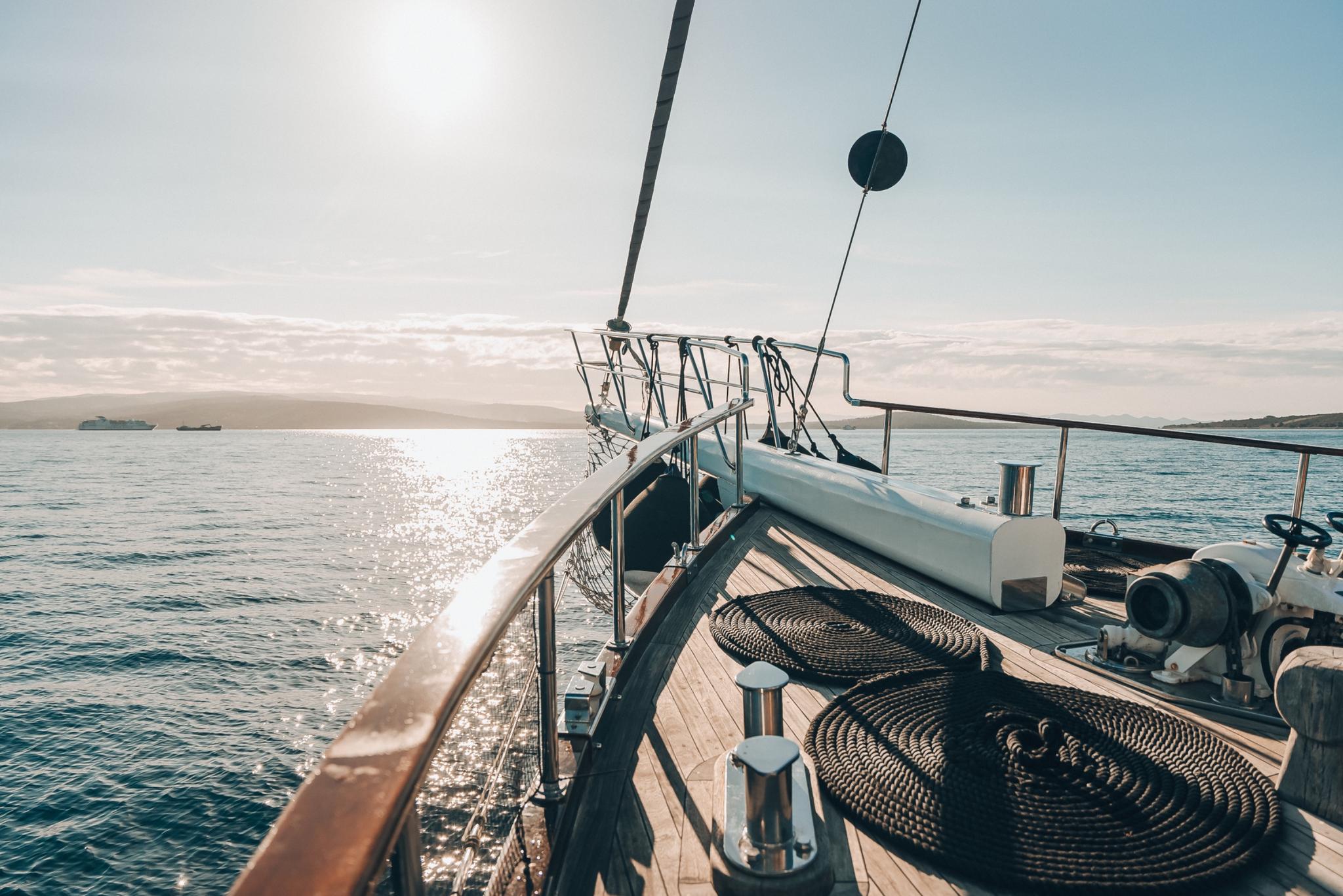 yacht bow deck showing coiled rope, teak decking, and rigging against ocean backdrop