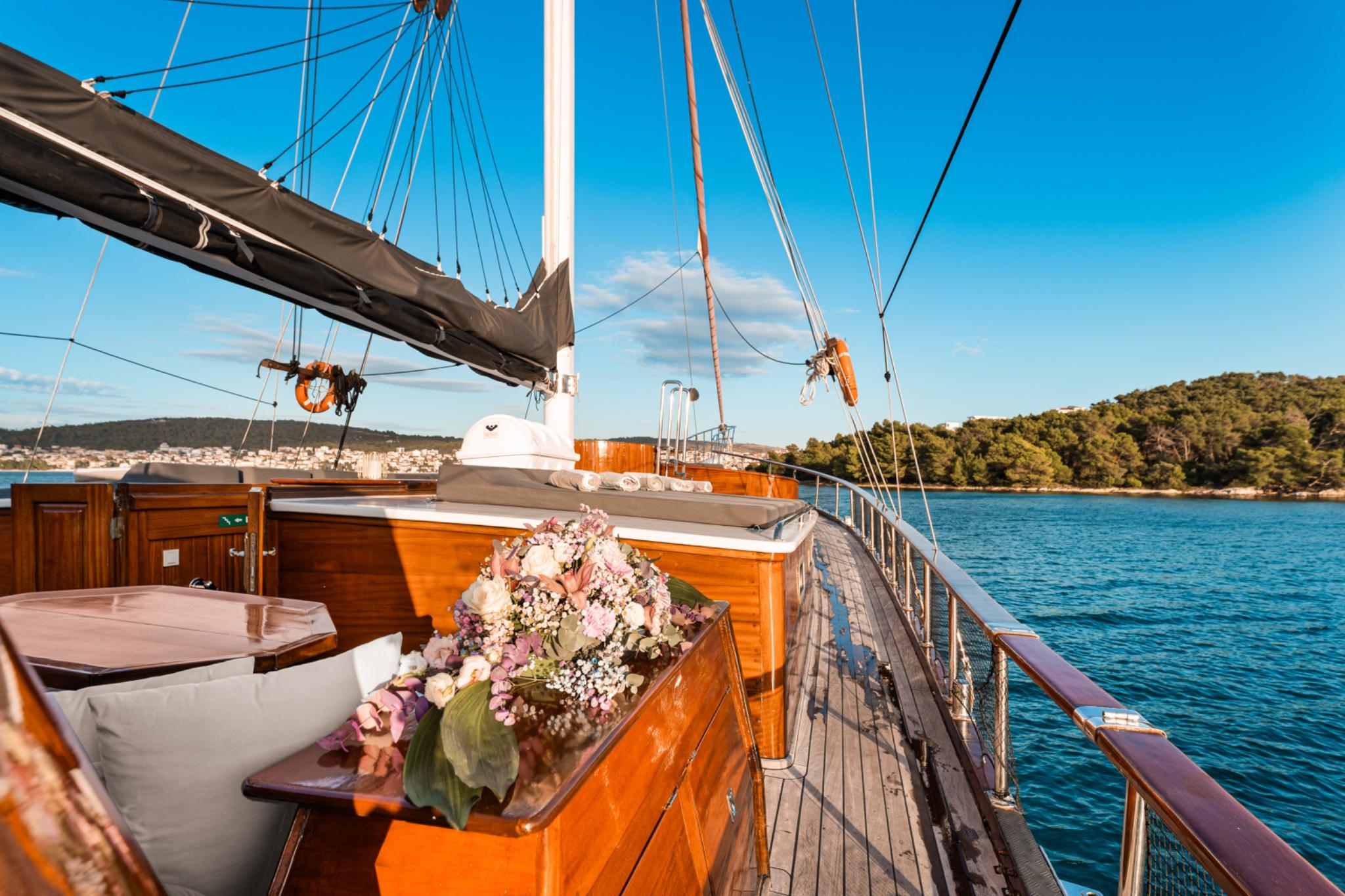 gulet aft deck with wooden dining table, white cushioned seating, and flower arrangement