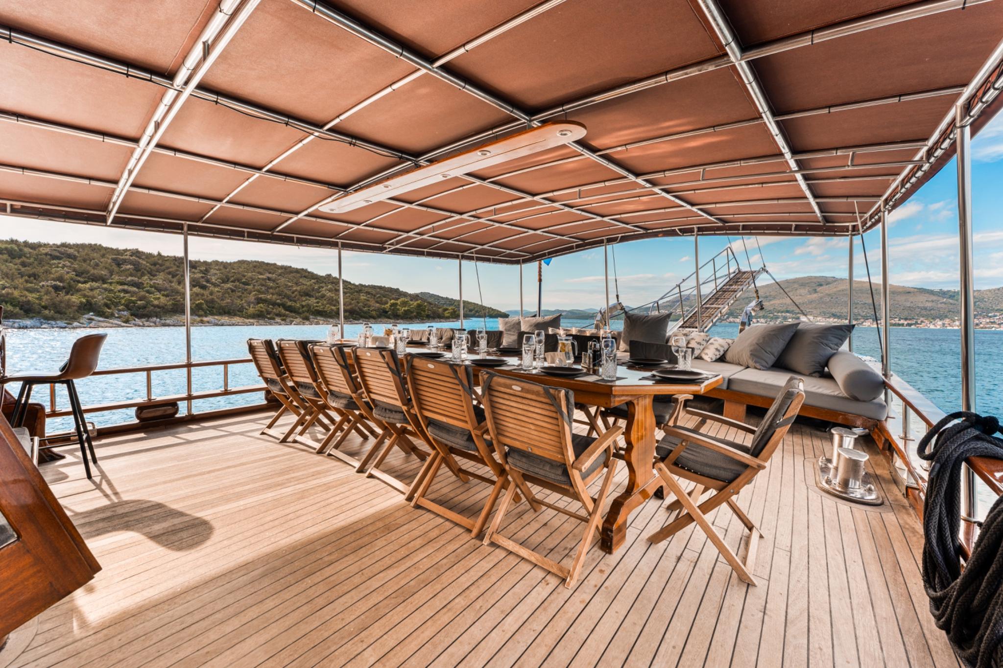 Covered aft deck dining area with wooden folding chairs, table settings and built-in seating