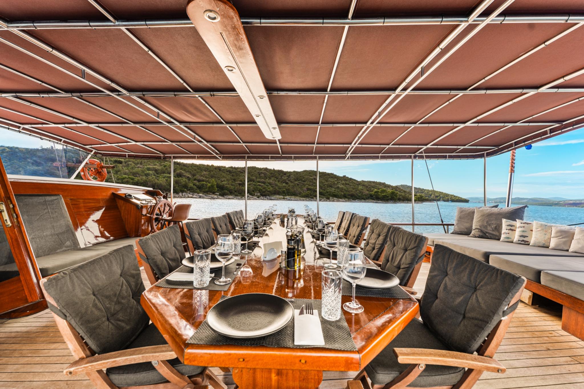 Gulet aft deck dining area with formal table setting under fabric awning overlooking coastal waters