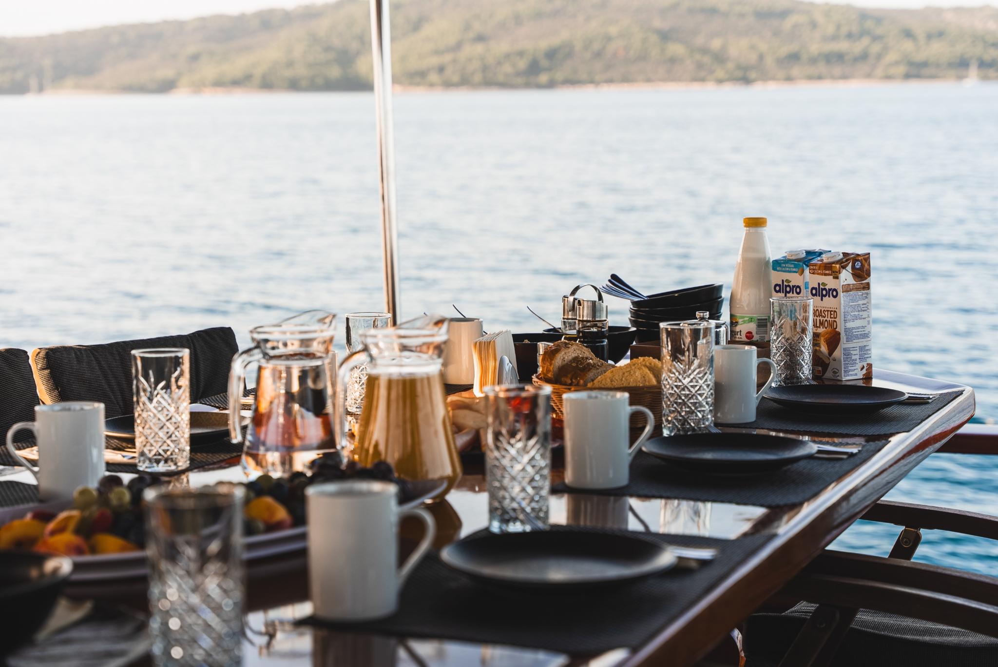 yacht breakfast table with coffee mugs, crystal glasses, bread basket and alpro milk cartons