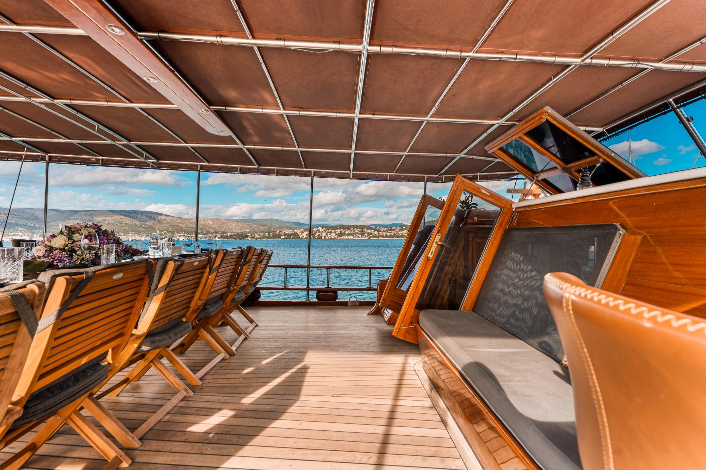 yacht upper deck with teak wooden loungers, glass windscreen, and coastal mountain views