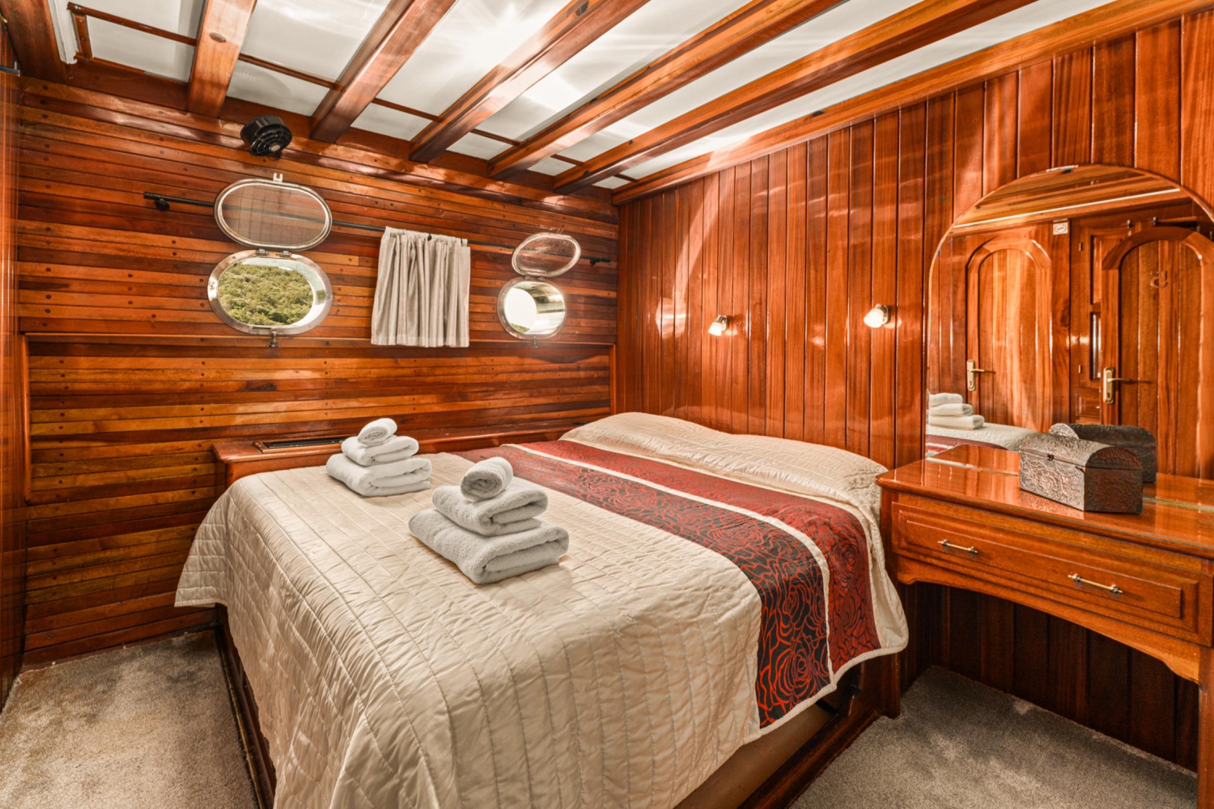 yacht guest cabin featuring double bed with beige quilted bedding and red decorative runner, built-in wooden wardrobes