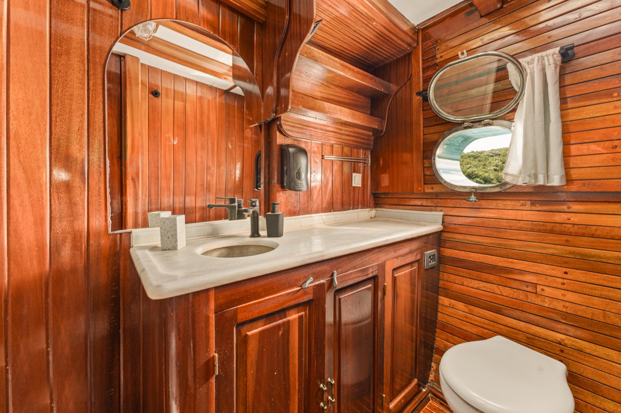 yacht bathroom with rich wood paneling, marble countertop vanity, oval mirror and porthole window