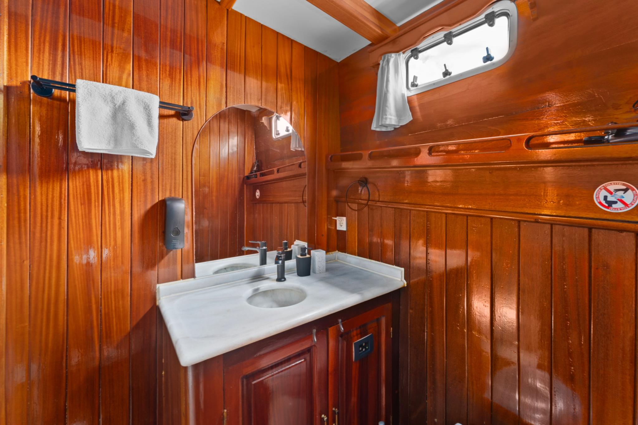 yacht bathroom featuring white marble sink, wooden cabinetry, towel rail and porthole window